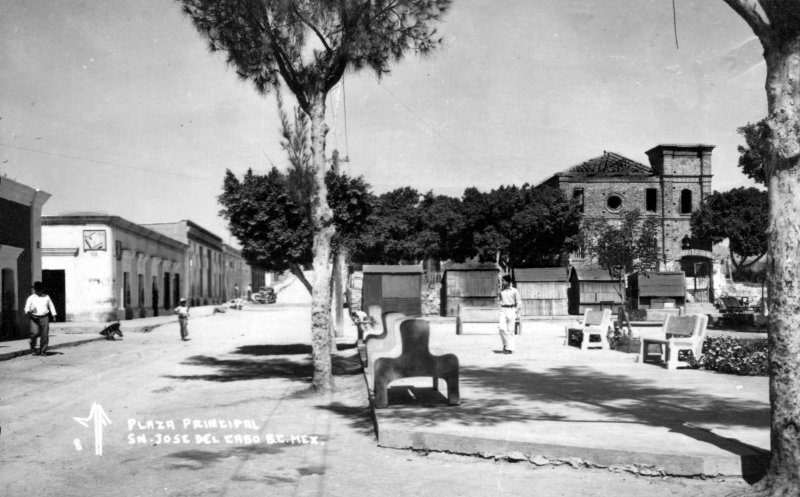 Black-and-white historical photograph of the main plaza of San José del Cabo, with benches, trees and the church in the background